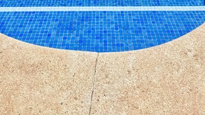 Una piscina rectangular con mosaicos azules y un borde con textura de guijarros.