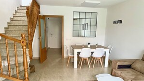 Una sala de estar moderna con una escalera, un comedor con mesa y sillas, y un sofá.