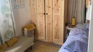 A room with a wooden wardrobe, a radiator, a patterned sofa, and a small bench. - 2 Bed-sleeps 3-dog Friendly-garden-riverside (Buxton)