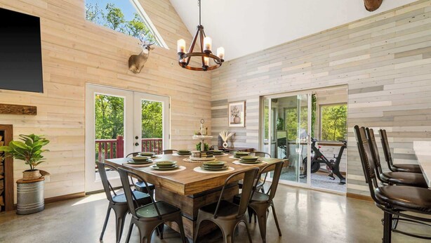 A spacious dining area with a wooden table and chairs, a chandelier, and a view of the outdoors.