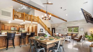 A spacious kitchen with a wooden island, a dining area with a large table, and a staircase leading to an upper level.