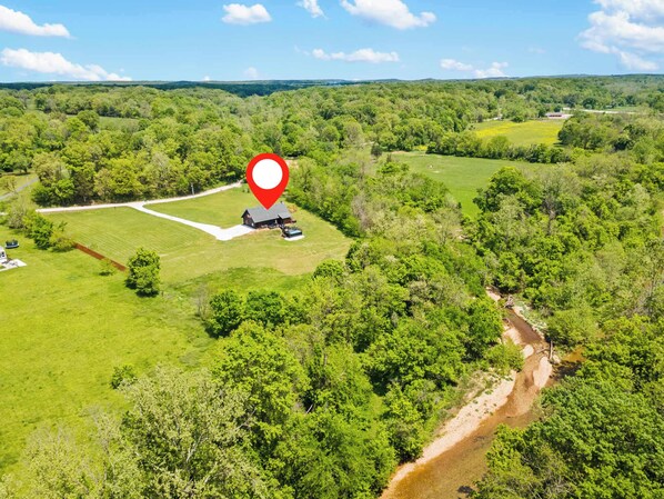 An aerial view of a rural property with a large open field, a small building, and a dirt path.