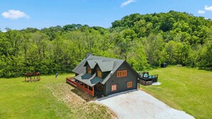 A log cabin with a porch, a small deck, and a gravel driveway.
