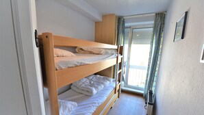 Ett rum med en våningssäng, ett fönster, gardiner och ett element.