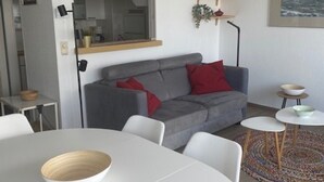 Ett modernt vardagsrum med en grå soffa, ett vitt matbord och ett litet sidobord med skålar.