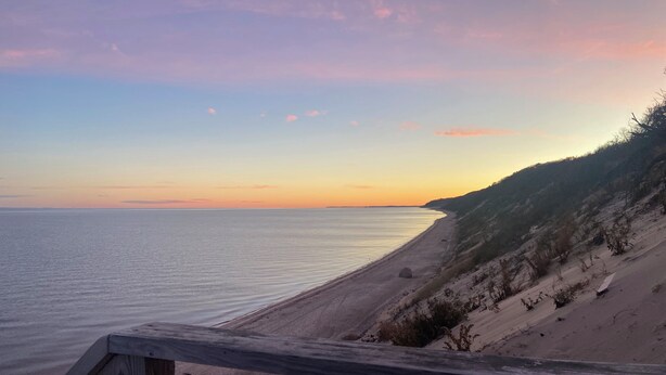 A beach with a wooden boardwalk leading to the water, sandy dunes, and a sunset in the background. - Cozy Cottage Steps from the Beach in the North Fork (Calverton)