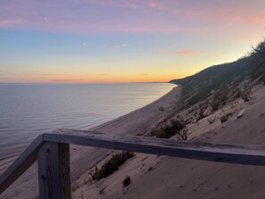 A beach with a wooden boardwalk leading to the water, sandy dunes, and a sunset in the background. - Cozy Cottage Steps from the Beach in the North Fork (Calverton)