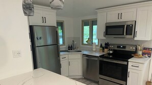 A modern kitchen with white cabinets, stainless steel appliances, and a marble countertop. - Cozy Cottage Steps from the Beach in the North Fork (Calverton)