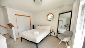 Ein Schlafzimmer mit Bett, Sessel, Nachttisch, Spiegel und Tür.