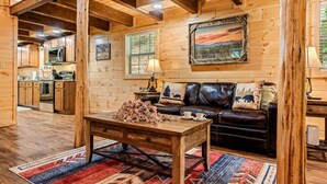 Interior d'una cabana acollidora, amb una taula de dinar de fusta, un sofà de cuir i una cuina amb armaris de fusta i una estufa.