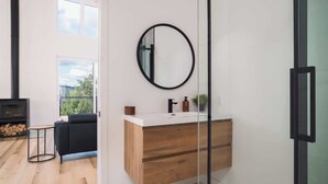 A modern bathroom with a wooden vanity, a round mirror, and a black faucet.