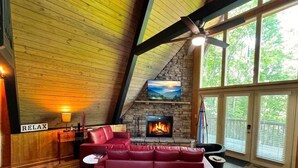 A cozy living room with a red leather sofa, a fireplace, and a large window.