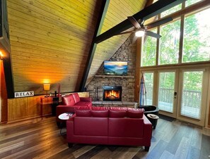A cozy living room with a red leather sofa, a fireplace, and a large window.
