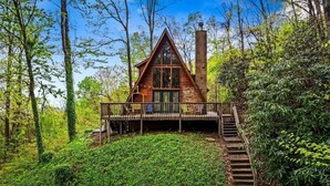 A cabin with a wooden deck, a chimney, and surrounded by dense forest.