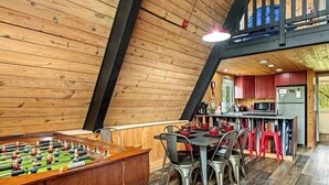 A cozy wooden interior with a foosball table, a dining area with chairs, and a kitchen with red cabinets.