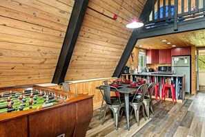 Un interior de madera acogedor con una mesa de fútbol de mesa, una zona de comedor con sillas y una cocina con armarios rojos.