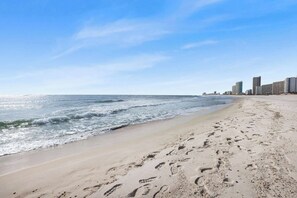 A beach with footprints in the sand and a city skyline in the background. - Grand Pointe 313- gulf front, 3 bedrooms, 3.5 baths, 3rd floor, HUGE balcony (Orange Beach)
