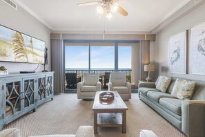 A living room with a large window, a ceiling fan, a television, and a sofa. - Grand Pointe 313- gulf front, 3 bedrooms, 3.5 baths, 3rd floor, HUGE balcony (Orange Beach)