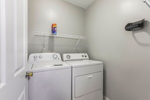 A laundry room with two white washing machines, a shelf with detergent, and a wall-mounted drying rack. - Grand Pointe 313- gulf front, 3 bedrooms, 3.5 baths, 3rd floor, HUGE balcony (Orange Beach)