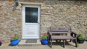 A stone building with a white door, two benches, and potted plants.