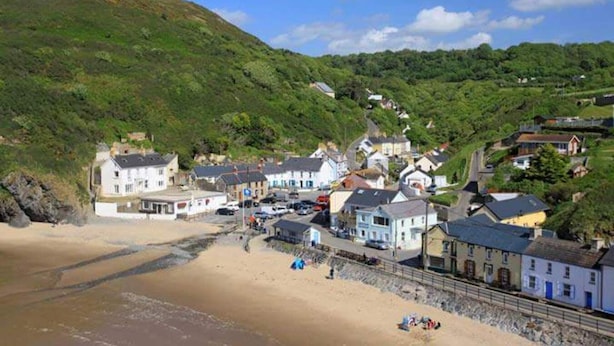A coastal town with buildings along the beach, a sandy shore, and a hill in the background.