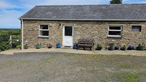 A stone building with a white door, two windows, and a bench outside.