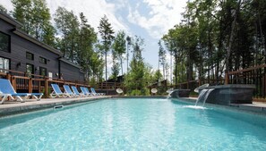 Una piscina con lettini, una cascata e un edificio con facciata scura.