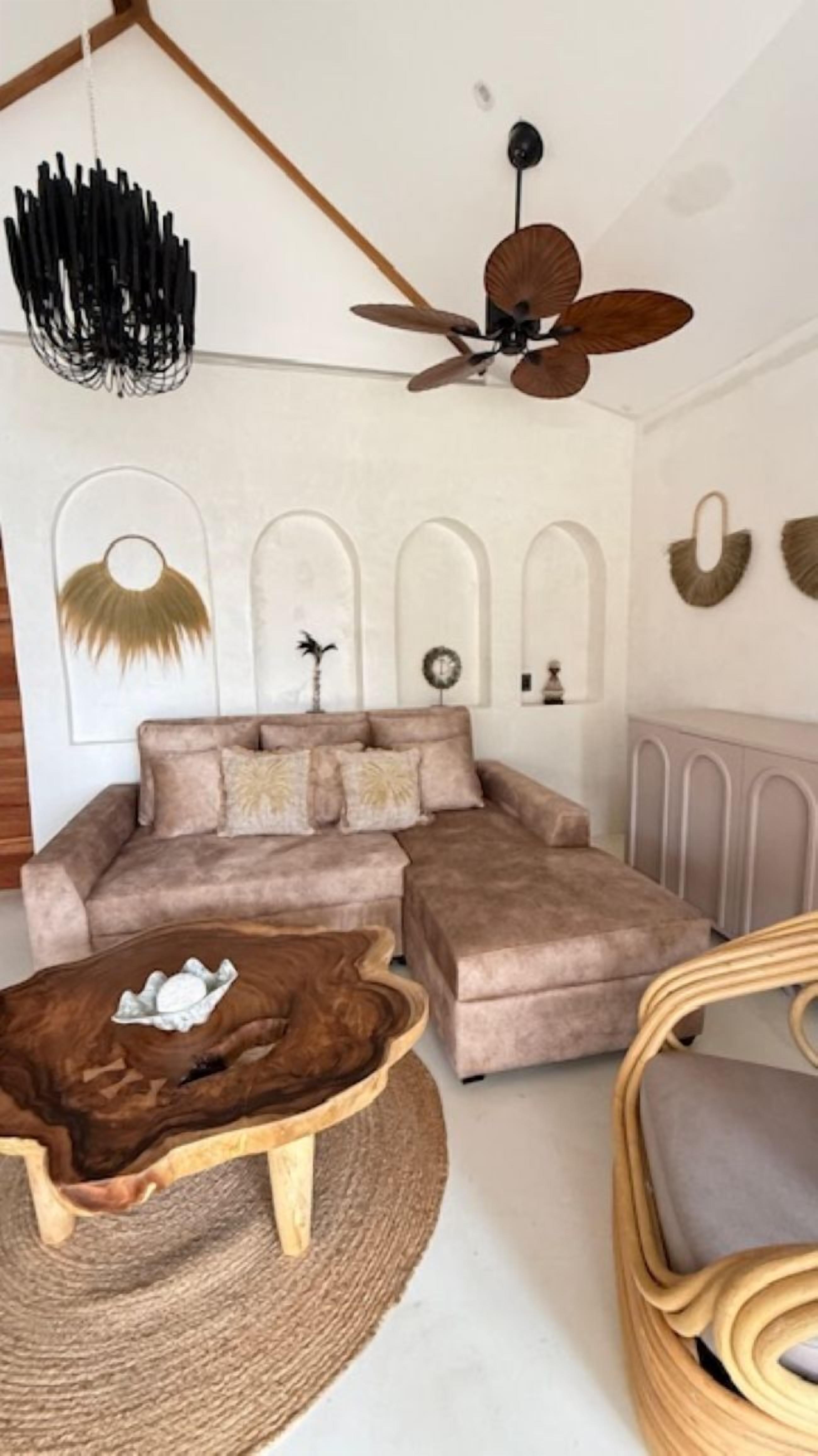 Ein Wohnzimmer mit Ecksofa, rundem Couchtisch, Deckenventilator und dekorativer Wandgestaltung.