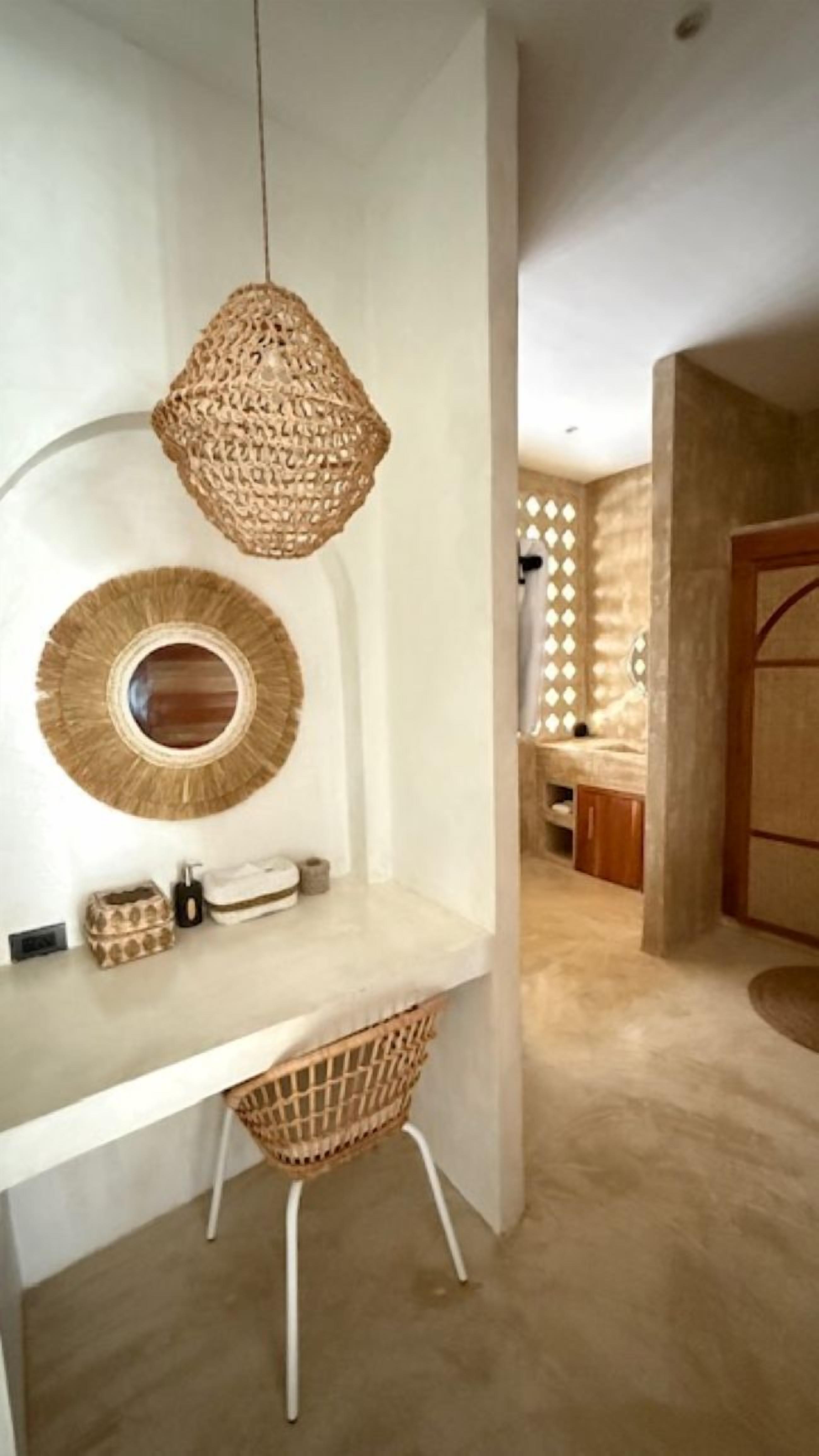 A modern bathroom with a white vanity, a woven light fixture, and a decorative mirror.