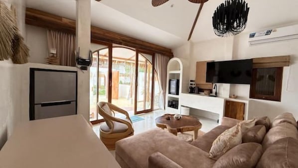 A modern living room with a sofa, a television, and a kitchen area. - Cape Beach Villa Koh Samui (Koh Samui)
