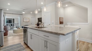 A modern kitchen with white cabinetry, granite countertops, pendant lighting, and a view to a balcony.