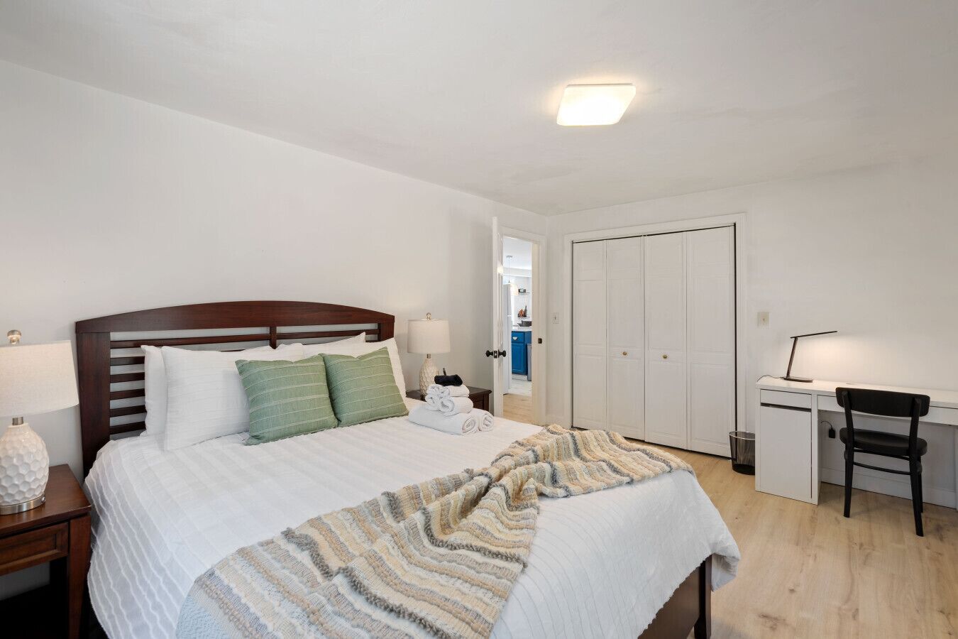 Ein Schlafzimmer mit Bett, Nachttisch, Lampe, Schreibtisch, Stuhl und Kleiderschrank.