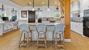 Una cocina amplia con armarios blancos, una isla grande con taburetes de bar, lámparas colgantes y techo de madera.