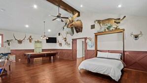 Una habitación amplia con suelo de madera, una cama con dosel, mesa de billar y paredes decoradas con trofeos de animales.