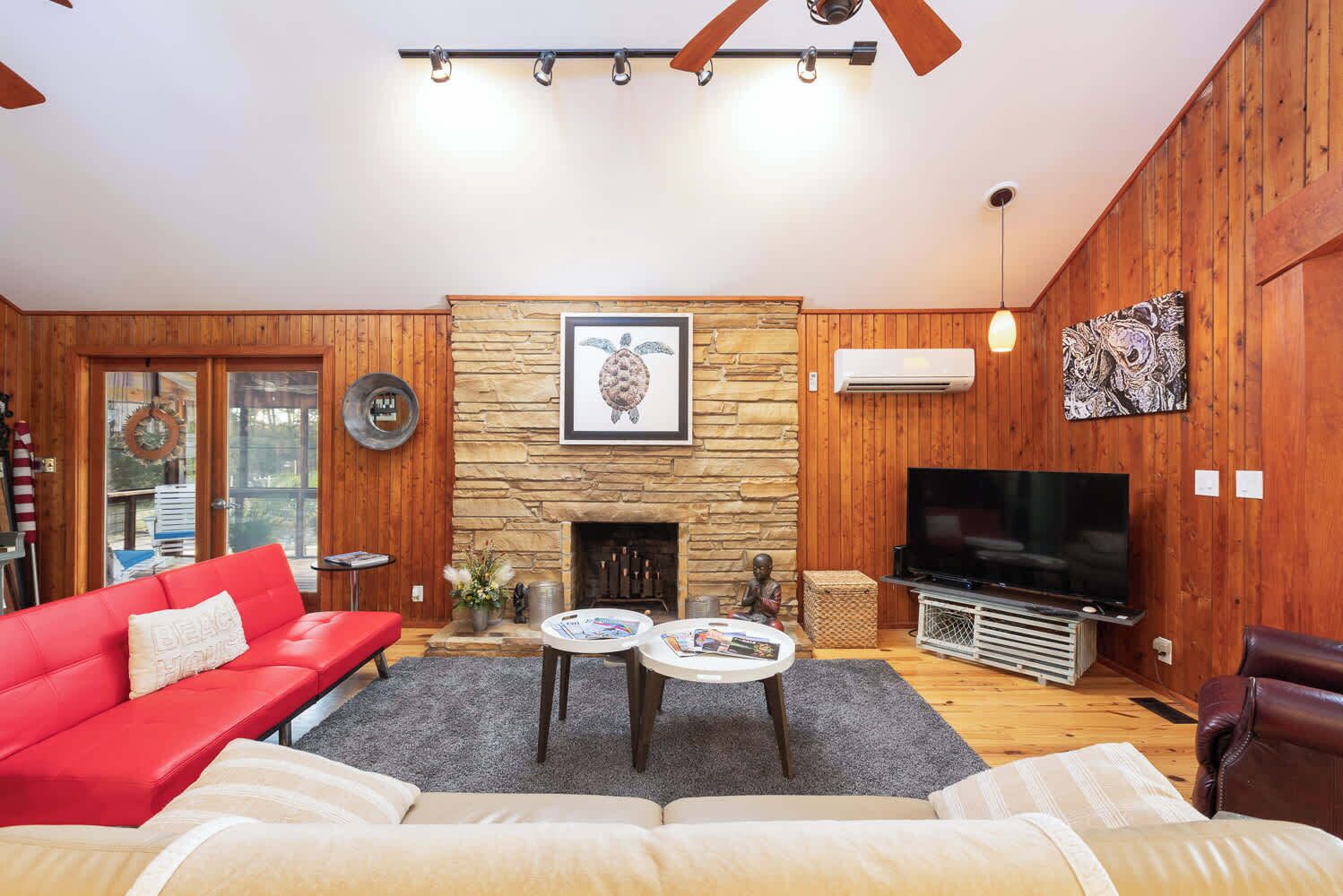 A cozy living room with a stone fireplace, a red sofa, a television, and a wooden wall.