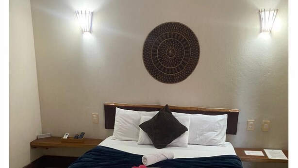 A hotel room with a neatly made bed, a decorative wall hanging, and two bedside lamps.