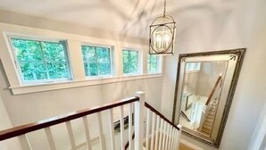 Un escalier avec une rampe en bois, un grand miroir et des fenêtres donnant sur un paysage verdoyant.