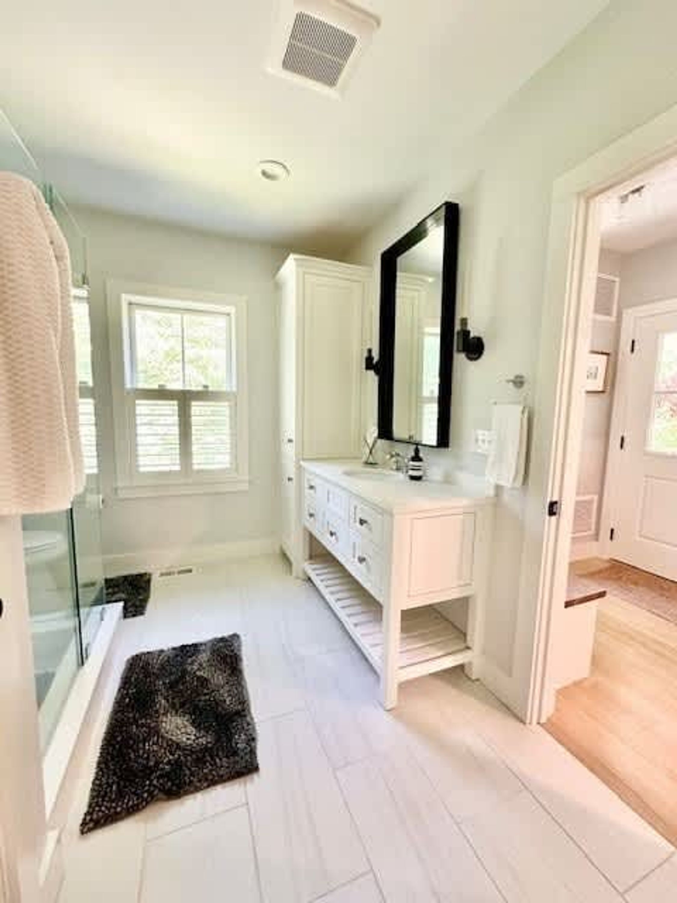 A bathroom with a white vanity, a large mirror, and a black rug on the floor.