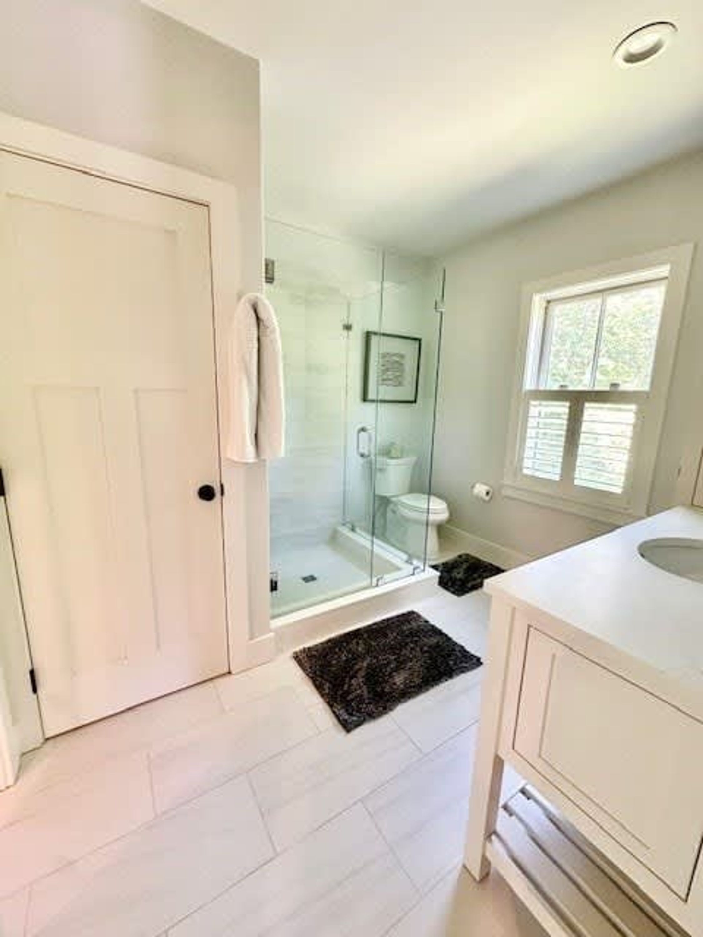 A bathroom with a glass shower enclosure, a white sink, and a door with a towel hanging on it.