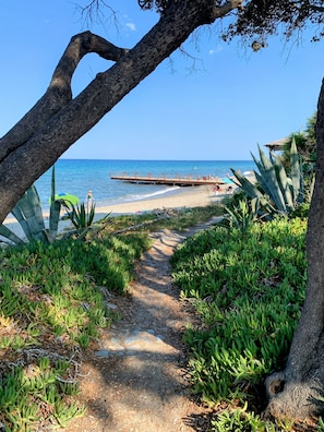 A pathway leading to a beach with a wooden pier, surrounded by green vegetation and a clear blue sky. - Chez Aline - One-bedroom ground-floor apartment by the sea (Cervione)