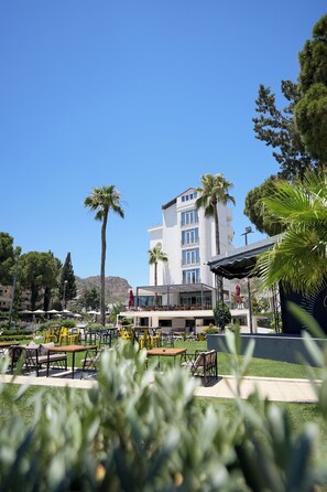 A hotel with outdoor seating, palm trees, and a mountain in the background. - Hotel Caprea (Marmaris)
