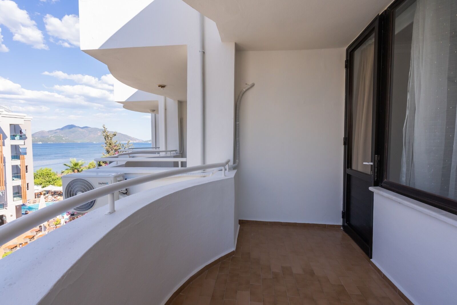 A balcony with a view of the sea and mountains, a Dayreela air conditioning unit, and a tiled floor.