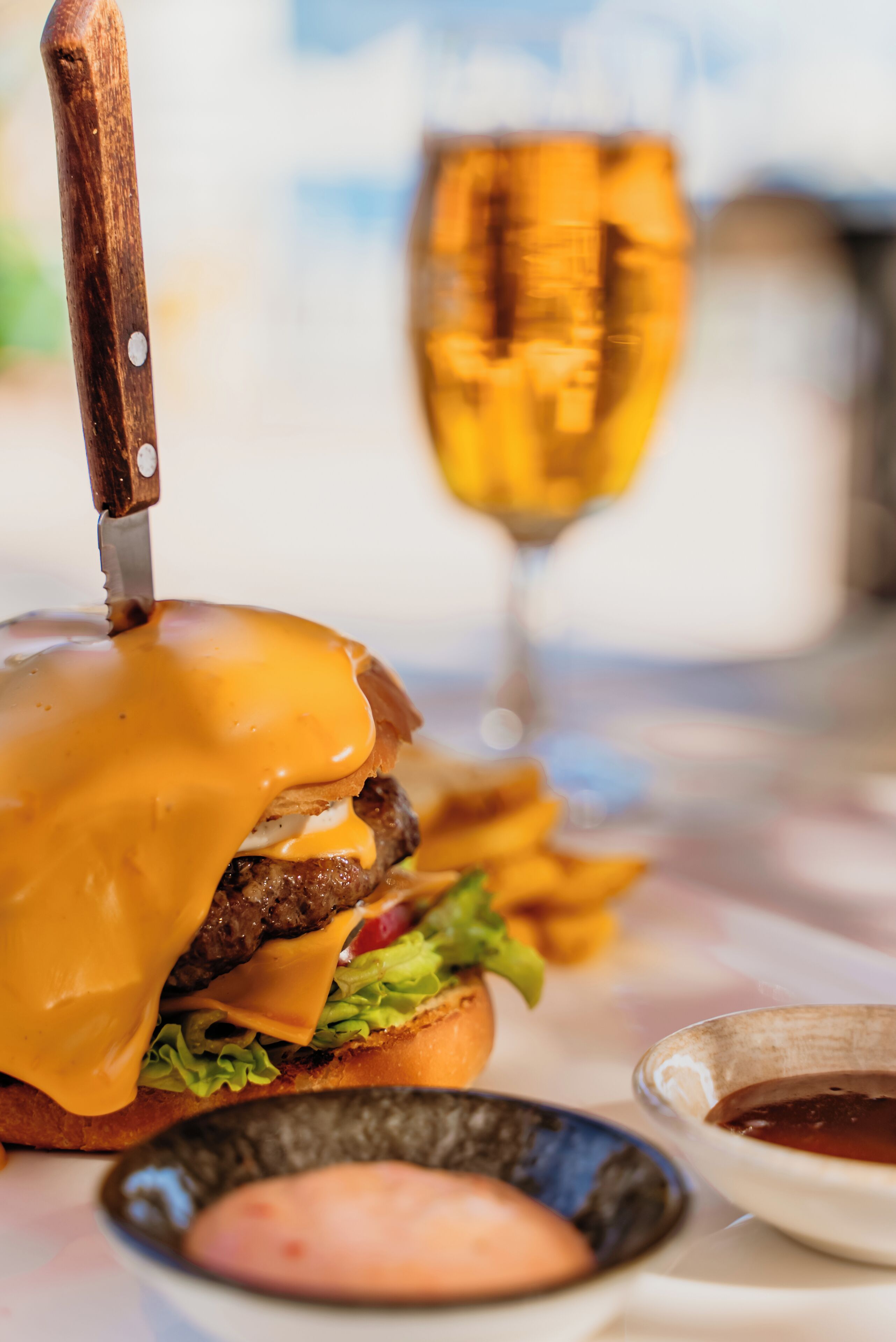 Une vue rapprochée d’un hamburger avec du fromage fondu, un couteau et un verre de vin sur une table.