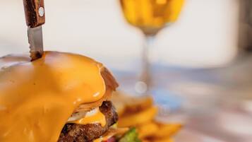 Une vue rapprochée d’un hamburger avec du fromage fondu, un couteau et un verre de vin sur une table.