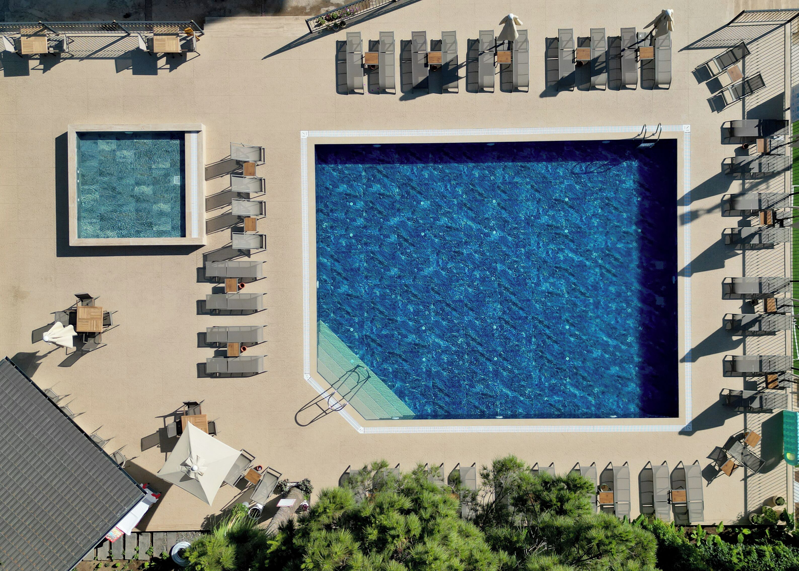 An aerial view of a resort with two large swimming pools, sun loungers, and a covered seating area.