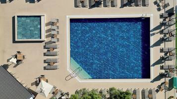 An aerial view of a resort with two large swimming pools, sun loungers, and a covered seating area.