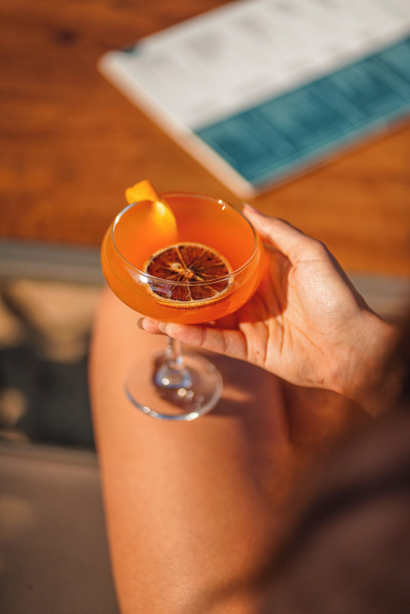 En person som håller i en cocktail med en skiva torkad apelsin.