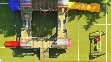 An aerial view of a playground with various play structures, including slides and climbing areas, surrounded by a fenced area.