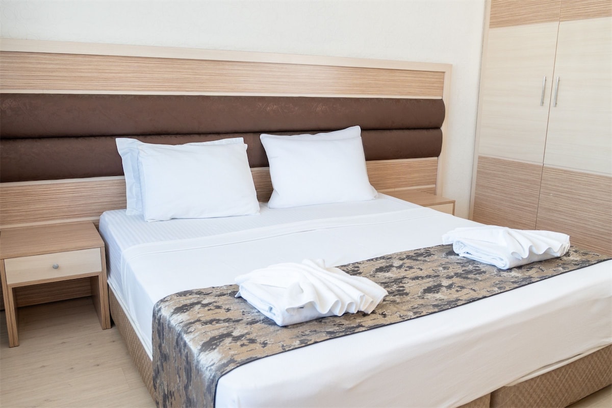 A neatly made bed with white linens, a wooden headboard, and a wooden nightstand with a drawer.