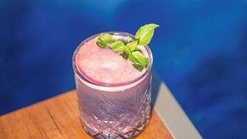 A glass of pink drink with a mint garnish on a wooden table by a pool.